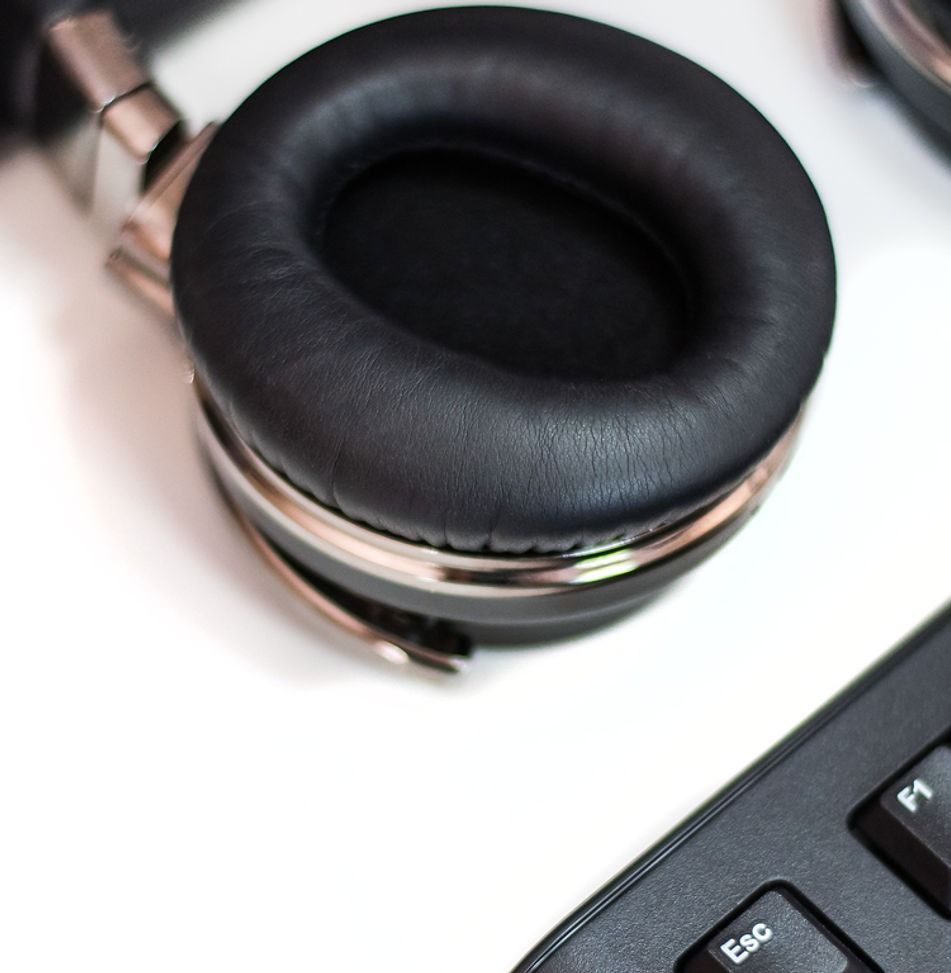 Black headphones with silver trim next to a black keyboard on a white surface.