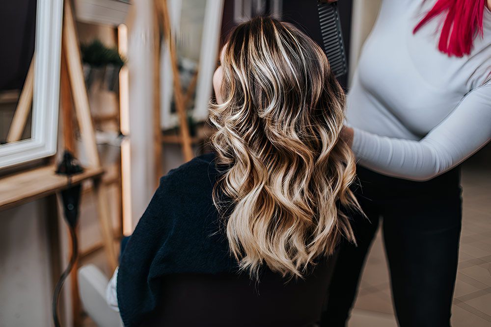 A Woman is Getting Her Hair Done by a Hairdresser in a Salon — Artistry of Hair in Redlynch, QLD