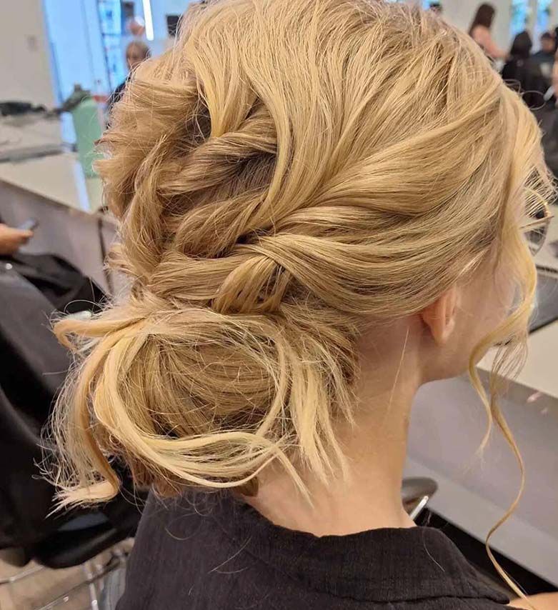 A Woman is Sitting in a Chair With Her Hair in a Bun — Artistry Of Hair in Redlynch, QLD