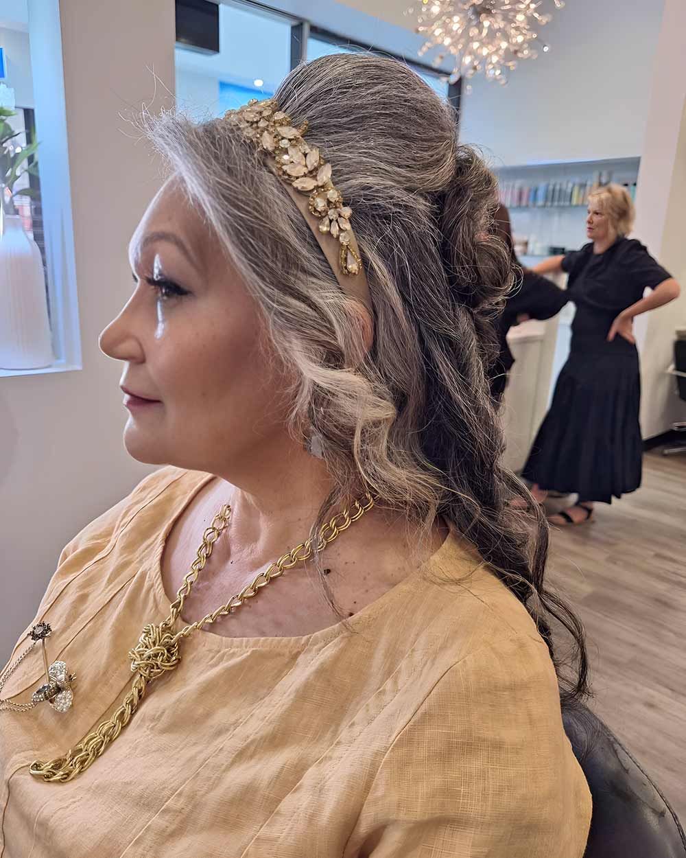 A Woman Wearing a Gold Necklace and a Gold Headband is Sitting in a Chair — Artistry of Hair in Redlynch, QLD