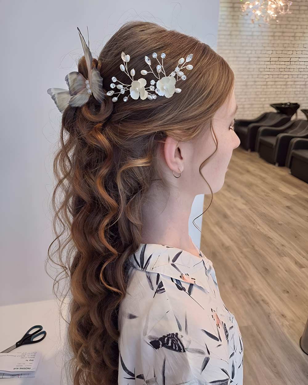 A Woman With Long Curly Hair is Wearing a Flower in Her Hair — Artistry of Hair in Redlynch, QLD