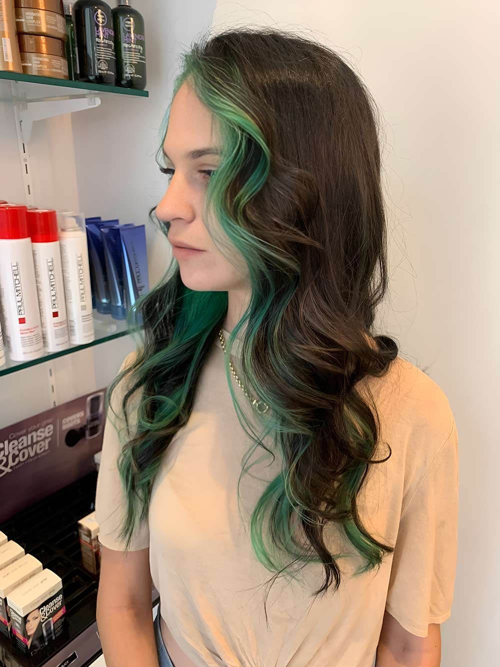 A Woman With Green Hair is Standing in Front of a Shelf of Hair Products — Artistry of Hair in Redlynch, QLD