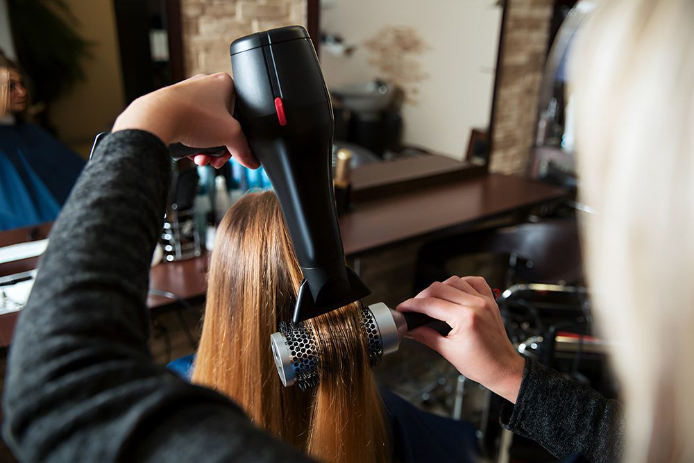 A Woman is Getting Her Hair Blow Dried by a Hairdresser in a Salon — Artistry of Hair in Redlynch, QLD