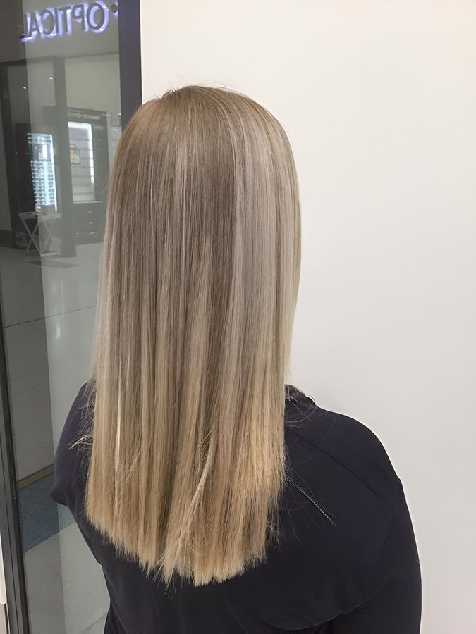 A Woman With Long Blonde Hair is Standing in Front of a Mirror — Artistry of Hair in Redlynch, QLD