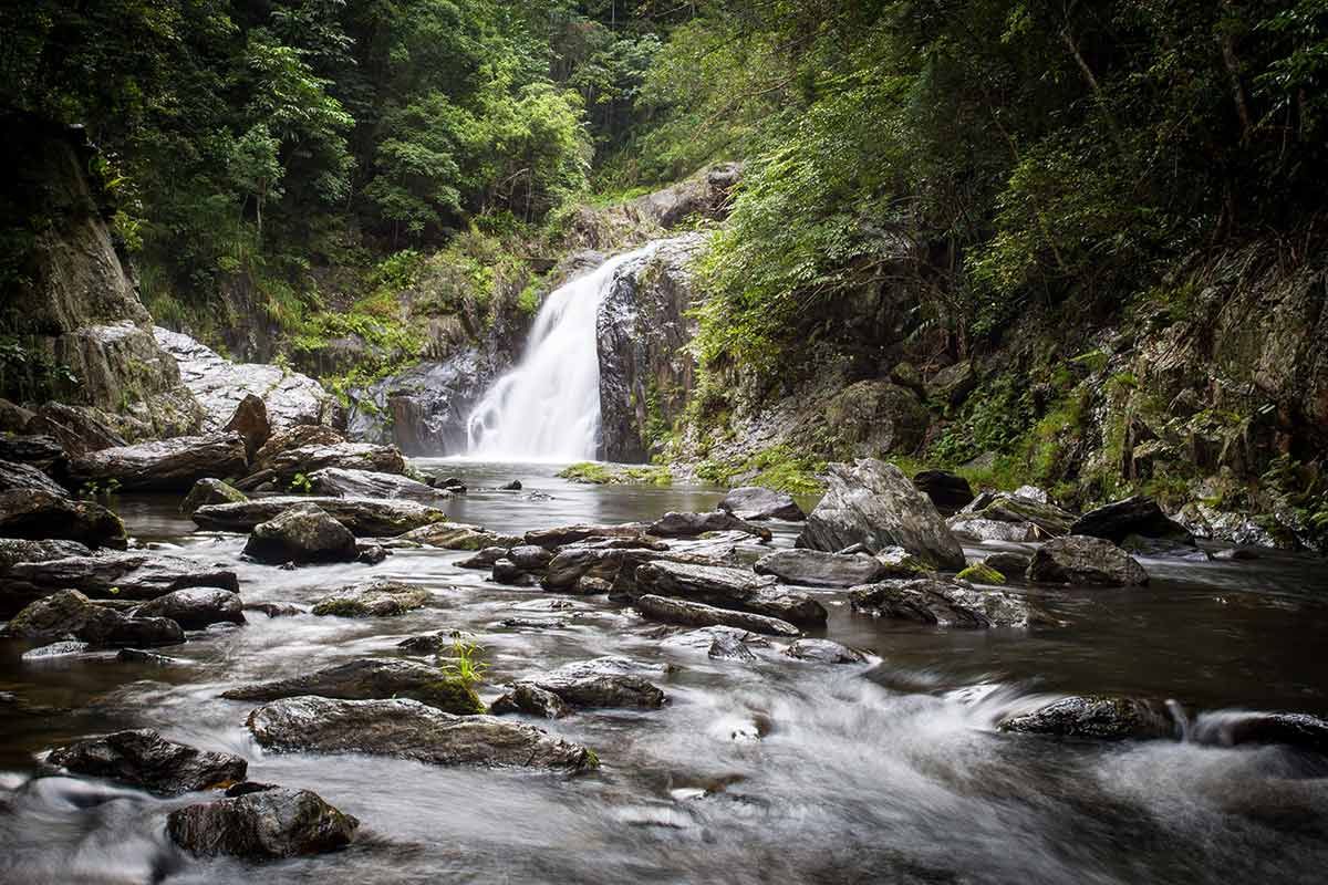A Waterfall is Surrounded by Trees and Rocks in the Middle of a River — Artistry of Hair in Redlynch, QLD
