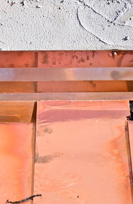 Primo piano di tegole arancioni sotto un muro di stucco bianco con piccole crepe e macchie.