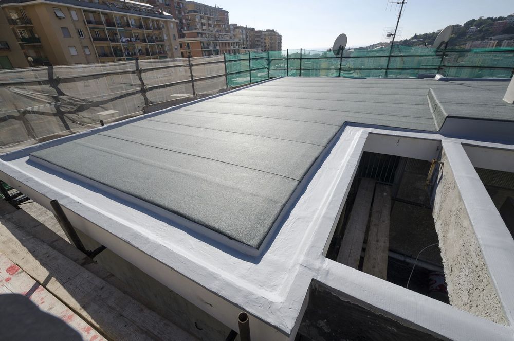 Tetto piano con membrana grigia, finiture bianche e, sullo sfondo, edifici in costruzione nelle vicinanze.