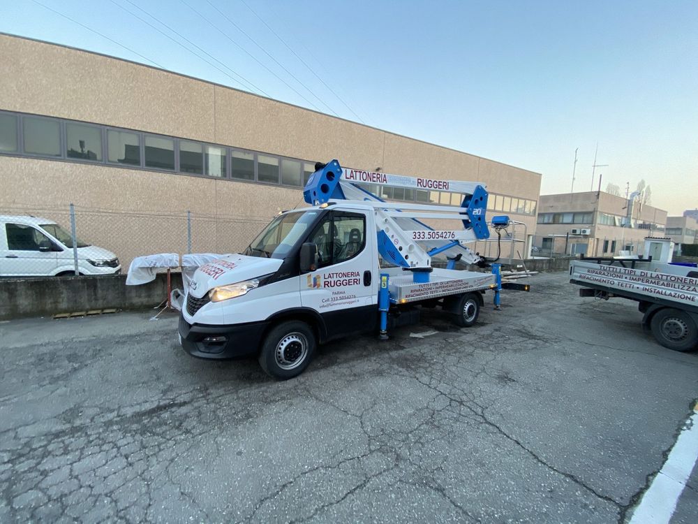 Un camion con piattaforma aerea bianca è parcheggiato in un'area industriale accanto a un edificio beige.