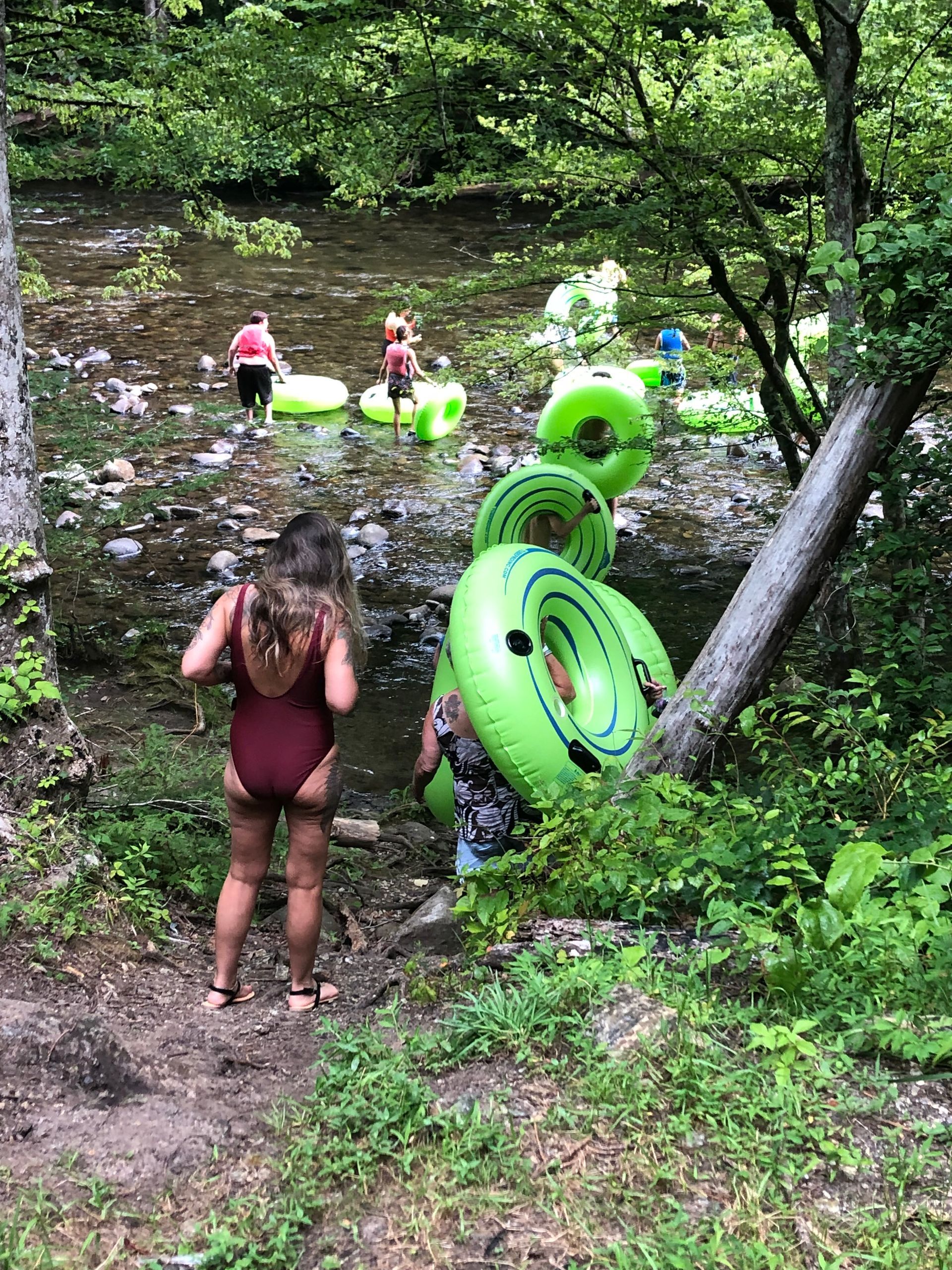 A woman in a red swimsuit is standing next to a river filled with green inner tubes.