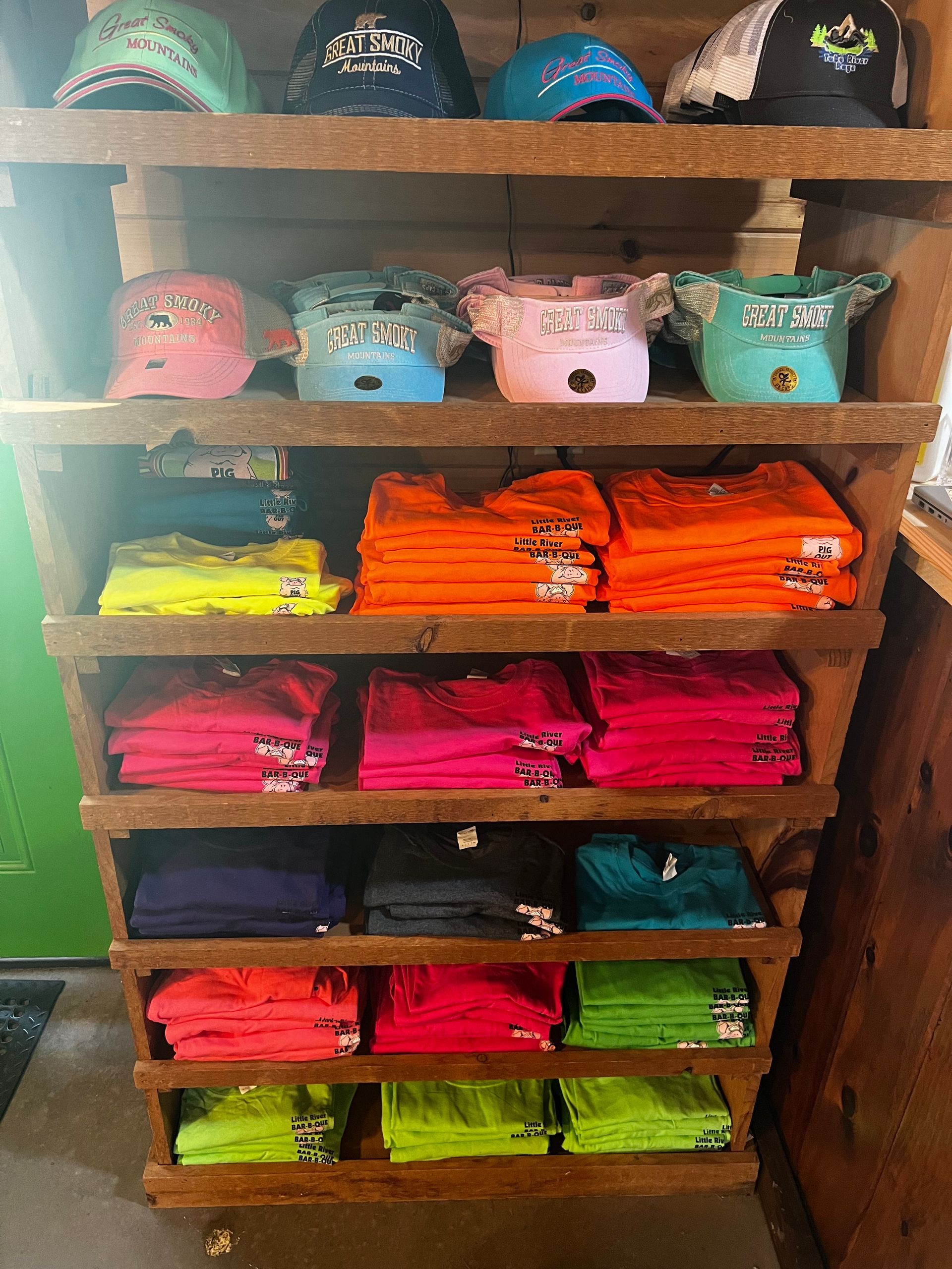 A wooden shelf filled with a variety of hats and t-shirts.