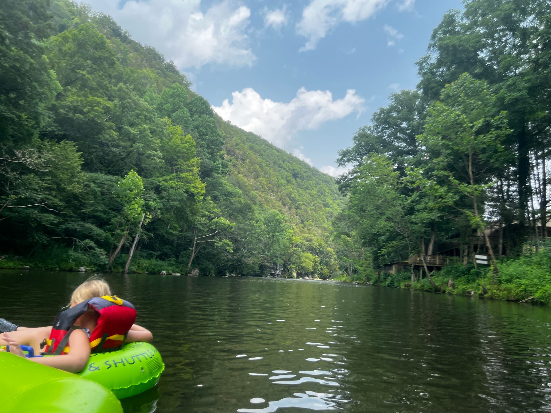 A child is floating down a river in a green tube.