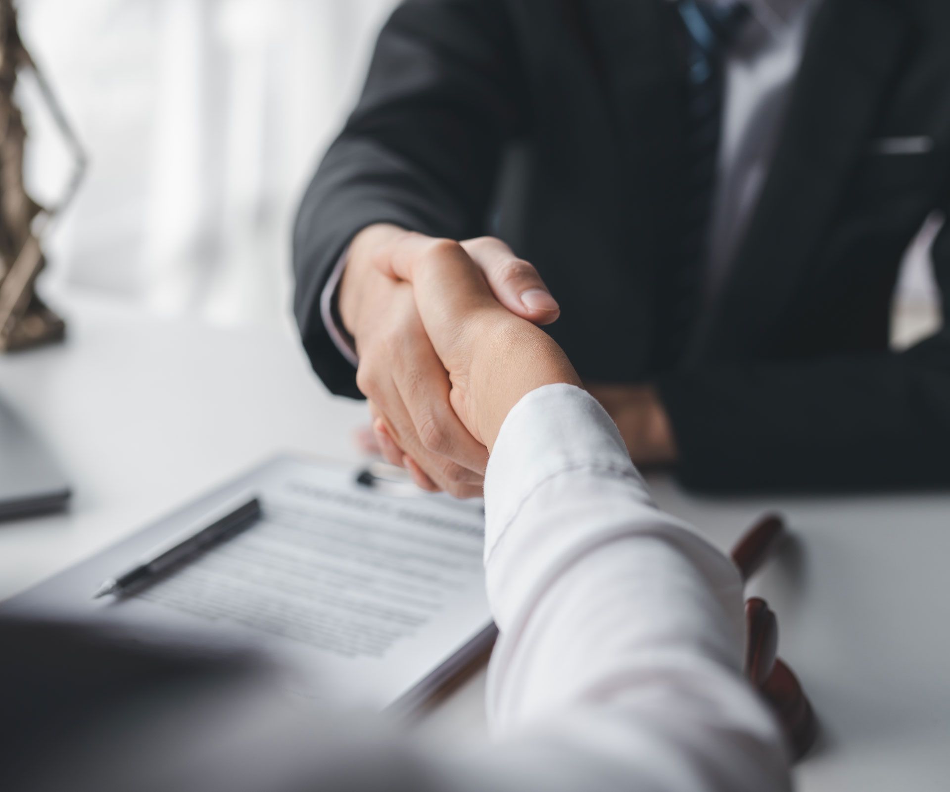 Two people shaking hands over a document at a desk.