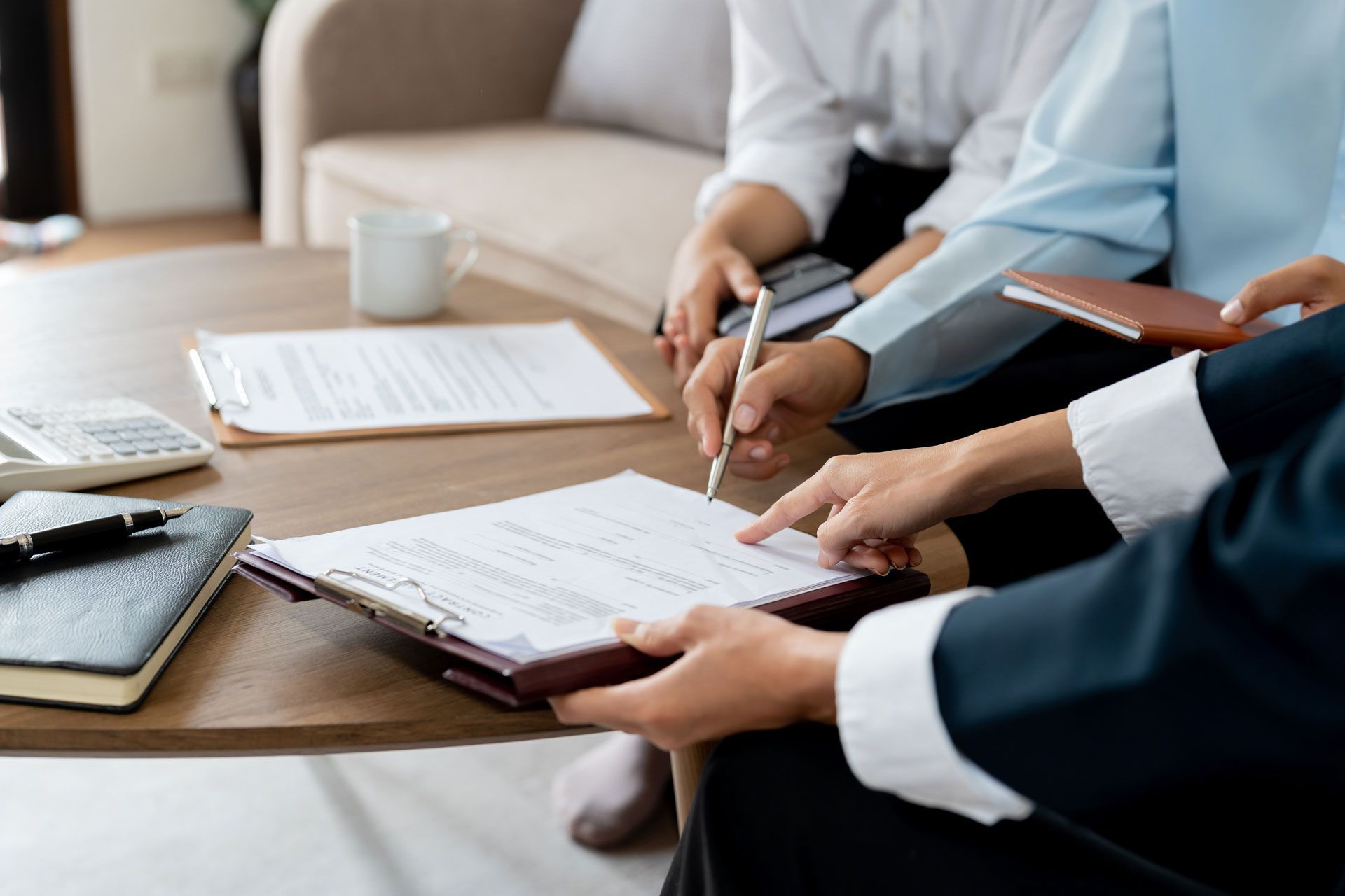 People reviewing and signing documents at a table. One person points, another writes with a pen.