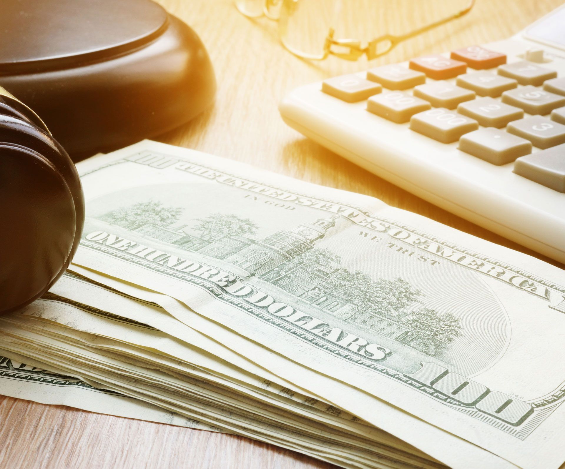 Stack of US dollar bills, gavel, and calculator on a wooden surface.