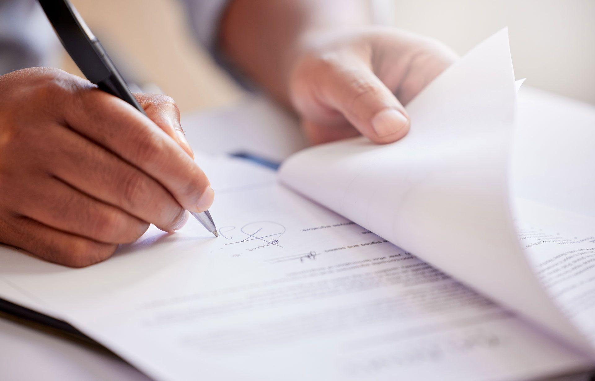 Person signing a document with a black pen, holding another page, close-up.