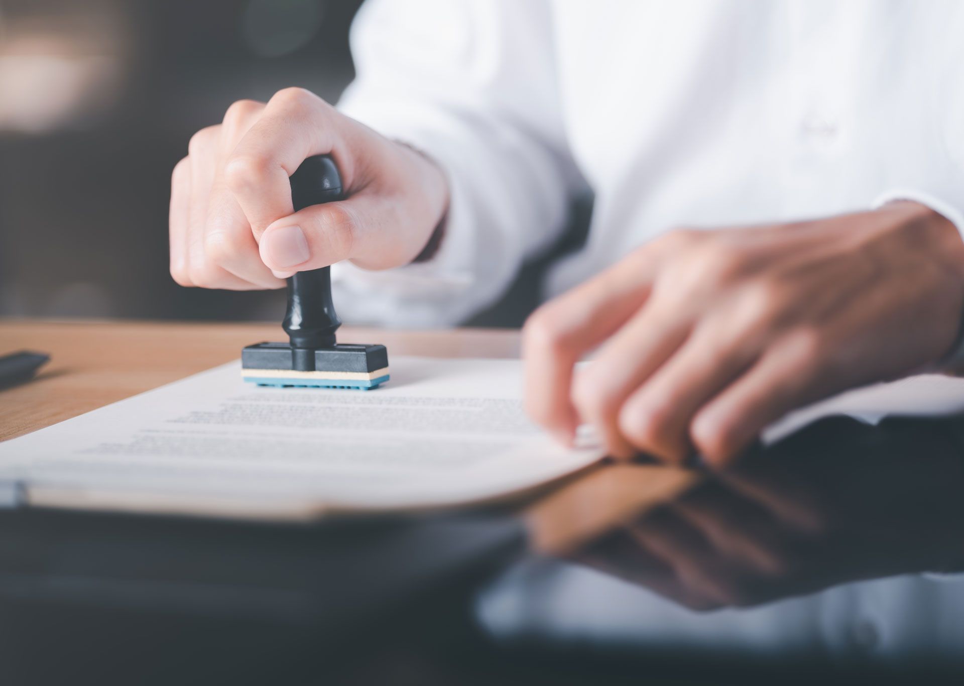 Person stamping a document with a black stamp, white shirt, and wood table.