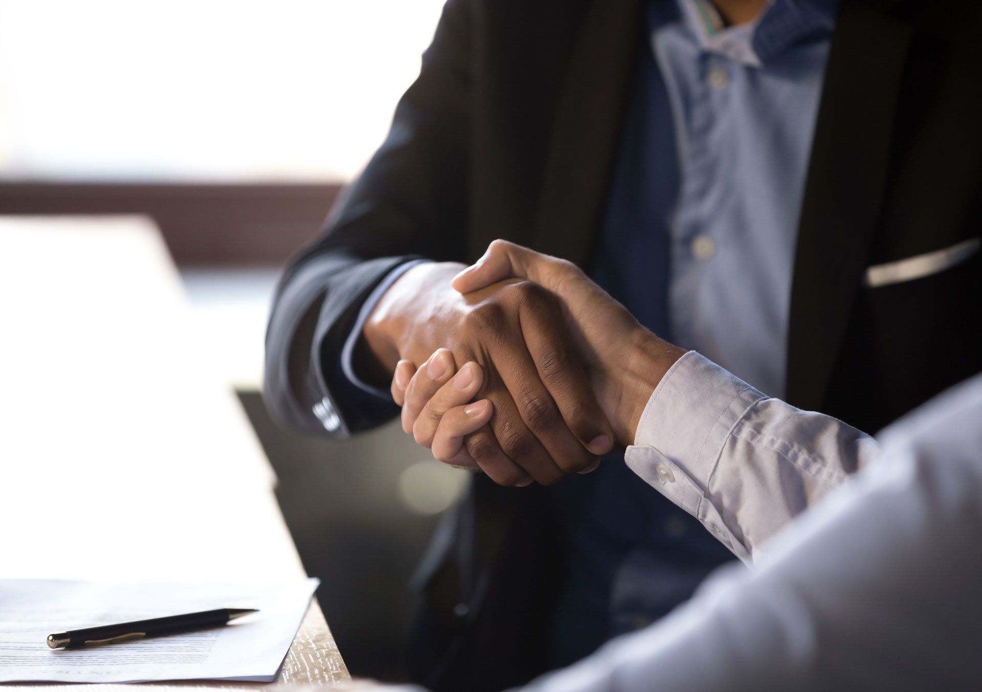 Two people in business attire shaking hands across a table, sealing a deal.