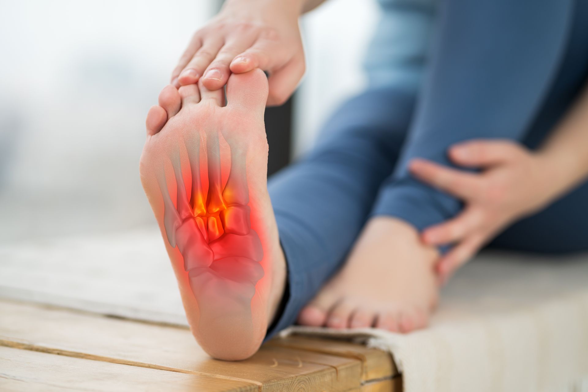 A person is sitting on a wooden bench holding their foot in pain.