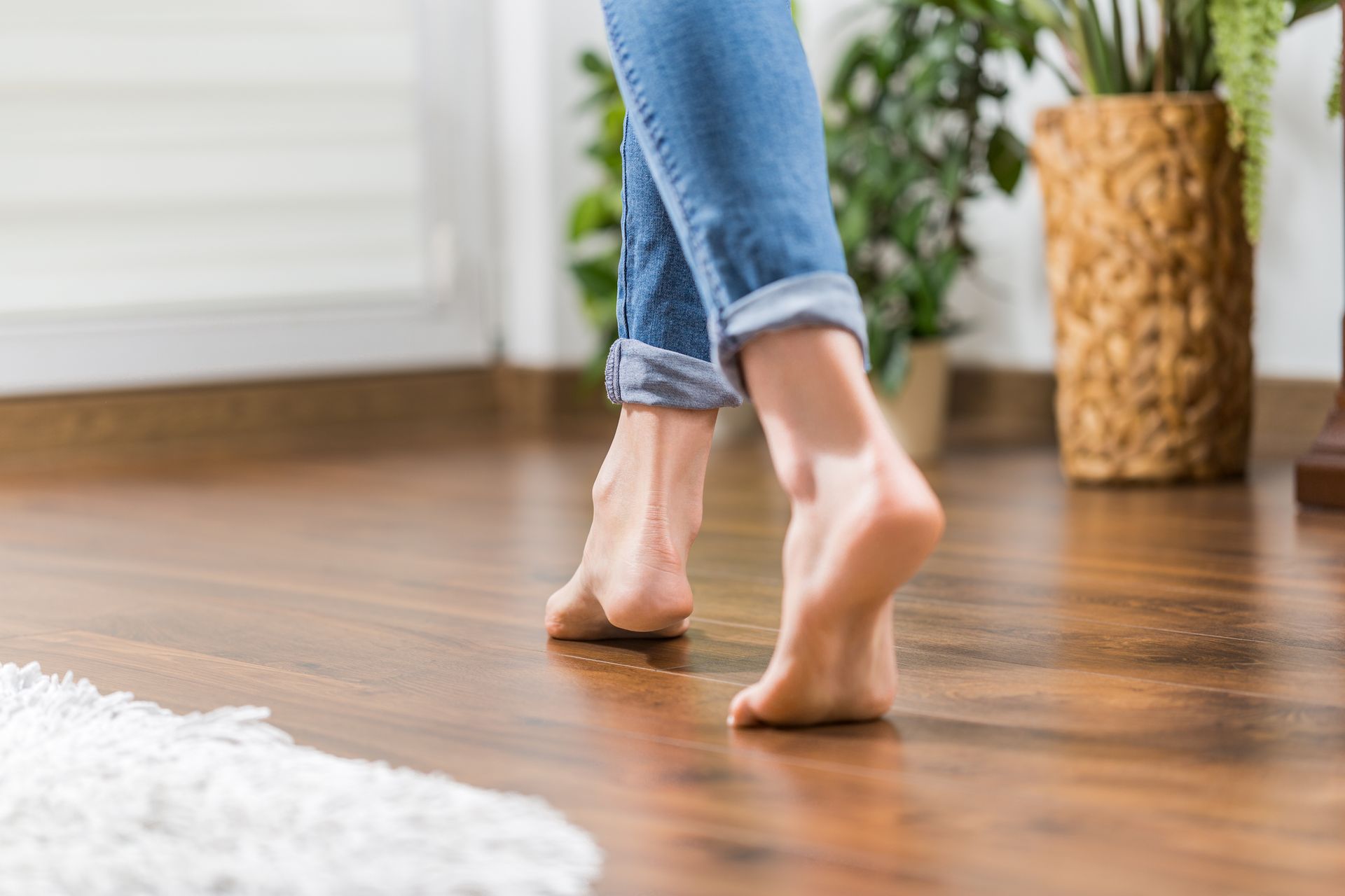Photo of woman's leg and feet walking barefoot on wooden floor.