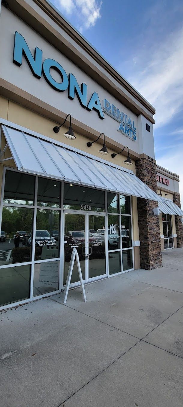 Exterior view of Nona Sushi and Korean BBQ restaurant in a strip mall. Blue signage, glass doors, and a sidewalk.