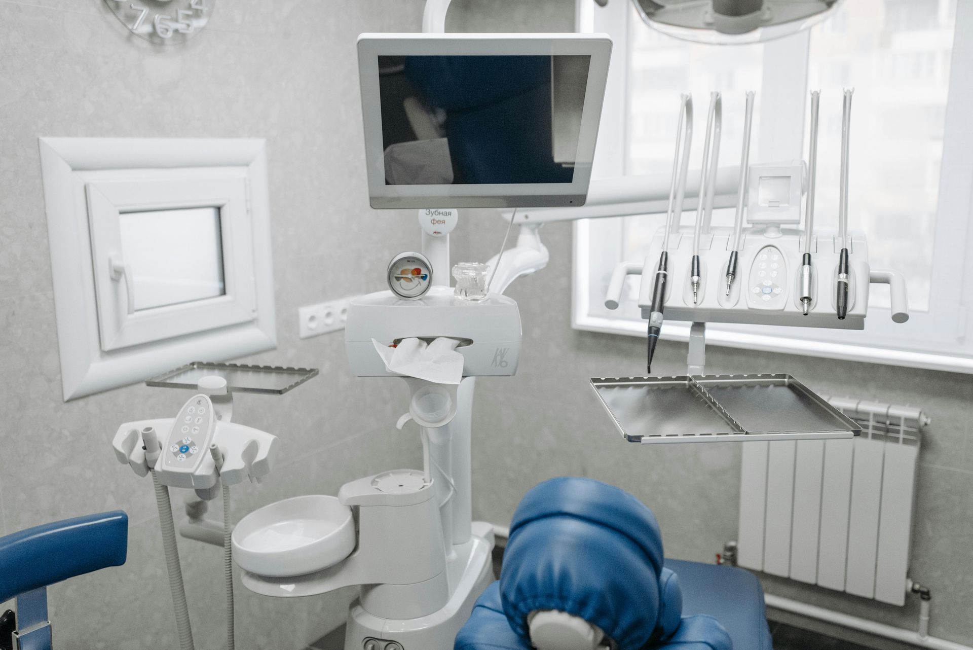 Dentist's office with dental chair, equipment, and monitor. Blue chair, white and gray equipment.