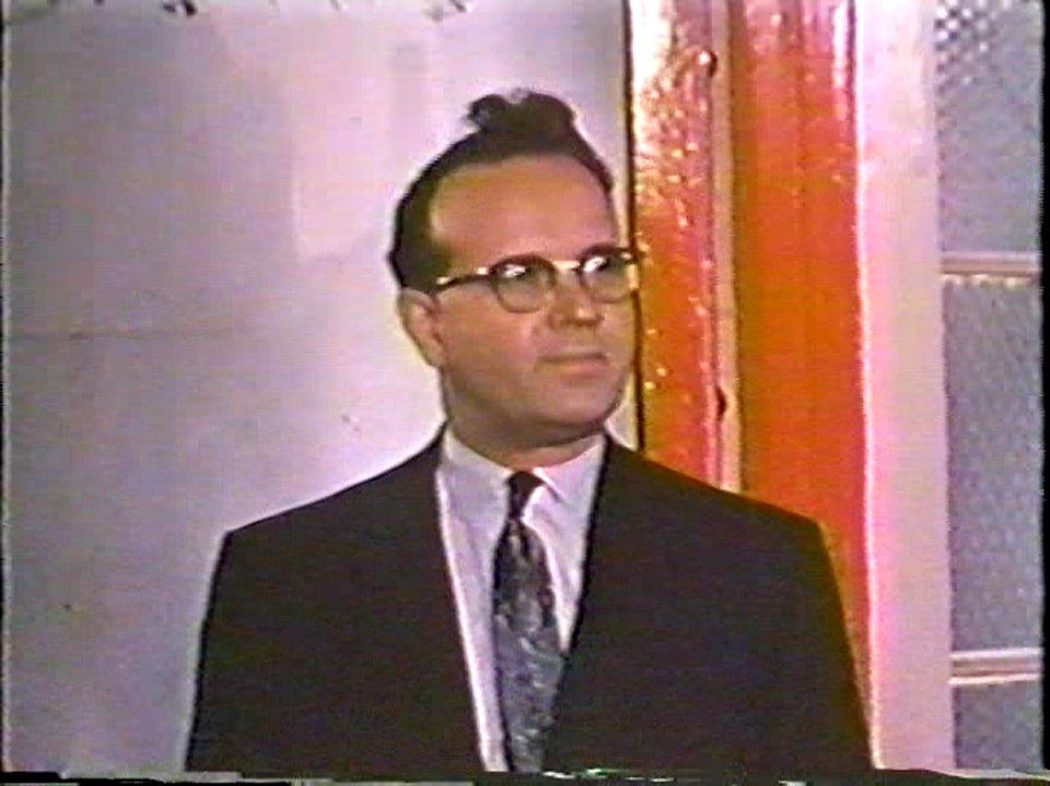 Doctor Matthew Dymond, Ontario Minister of Health from 1958-1969, during a visit to the Ontario Hospital School, Orillia. Dymond became the president of the Resperin Corporation in 1970, the same year that Resperin was found to be toxic. He is a round faced man with large round glasses and his dark hair swept up in an unusual way. Image from the government propaganda film One On Every Street.