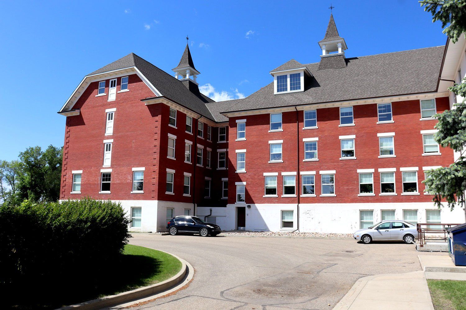 The main building of the Michener Centre in Red Deer, Alberta. It is a four storey red brick building with a peaked roof and two spires. The Michener Centre is the only large institution for people with intellectual/developmental disabilities in Canada that has no planned closure date. Image taken by Jason Woodhead, licensed under Creative Commons 2.0 (https://creativecommons.org/licenses/by/2.0/).