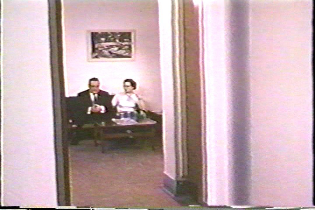 A staged scene from the propaganda film One On Every Street, showing a visiting room at the Ontario Hospital School, Orillia. The room is furnished with a coffee table and a small couch. Above this is a single painting hanging on the far wall. Until the 1970s, this was the only part of the institution that outsiders were permitted to see. Image from the government propaganda film One On Every Street.