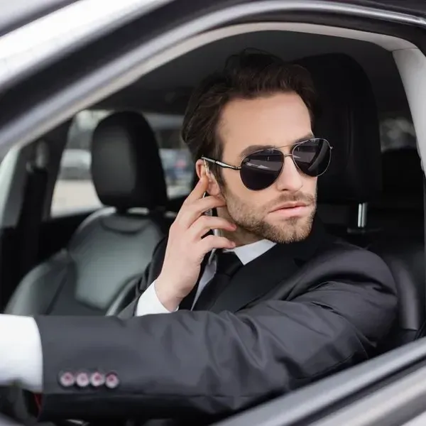 A man in a suit and tie is wearing sunglasses while driving a car