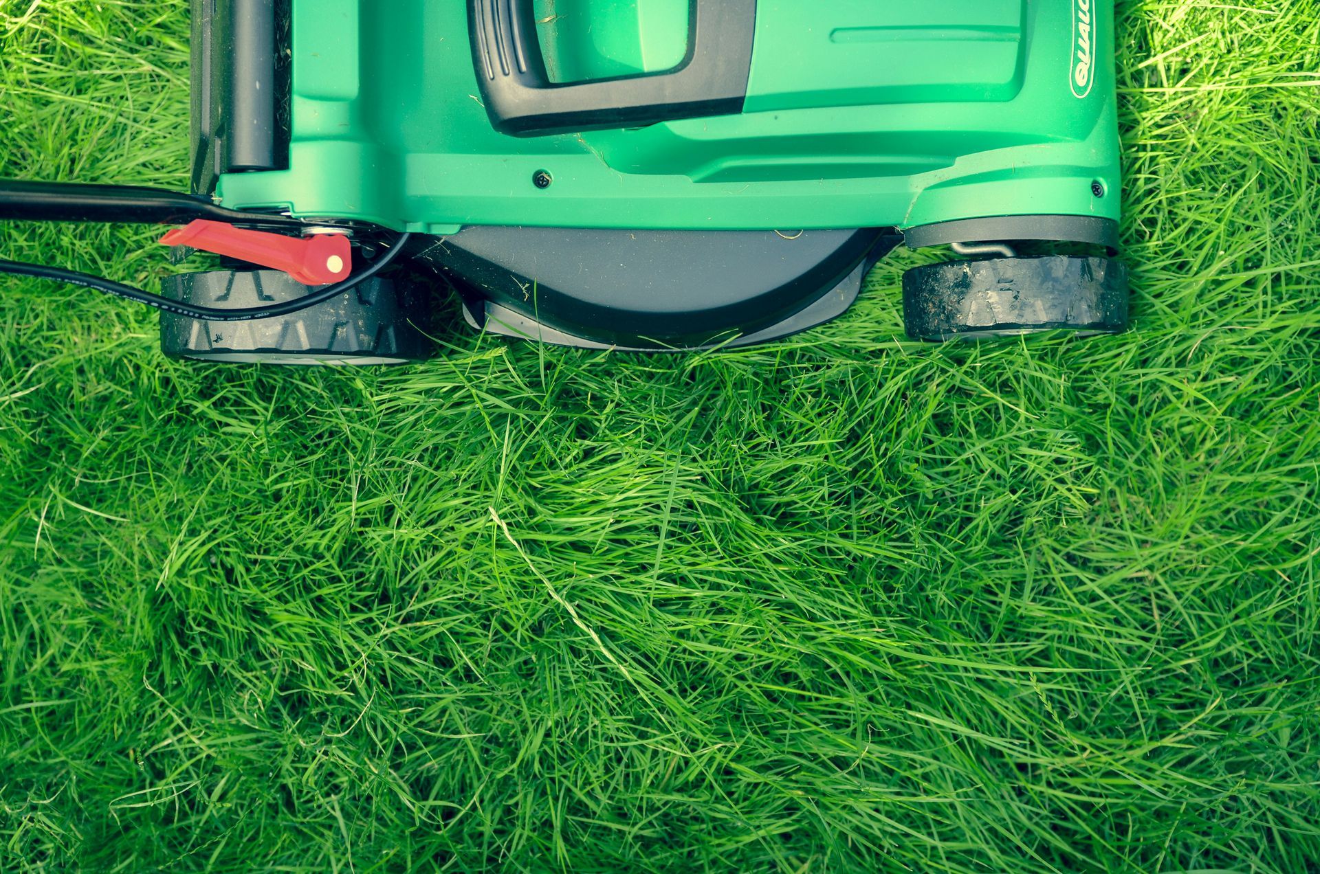 A green lawn mower is cutting a lush green lawn.