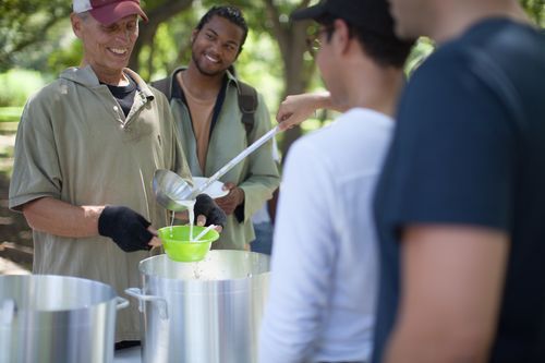 People serving food from large pots outdoors.