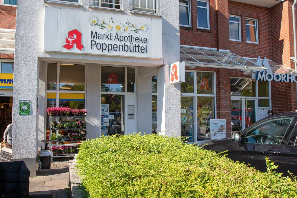 Außenansicht der Markt Apotheke Poppenbüttel, einer Apotheke mit einem roten „A“-Logo und Blumenkästen.