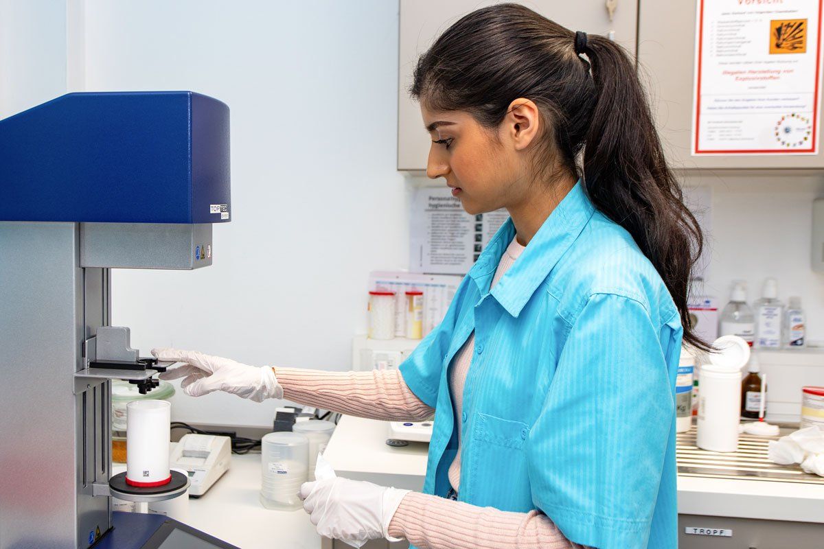 Eine Person im blauen Laborkittel bedient Laborgeräte in einem Labor.