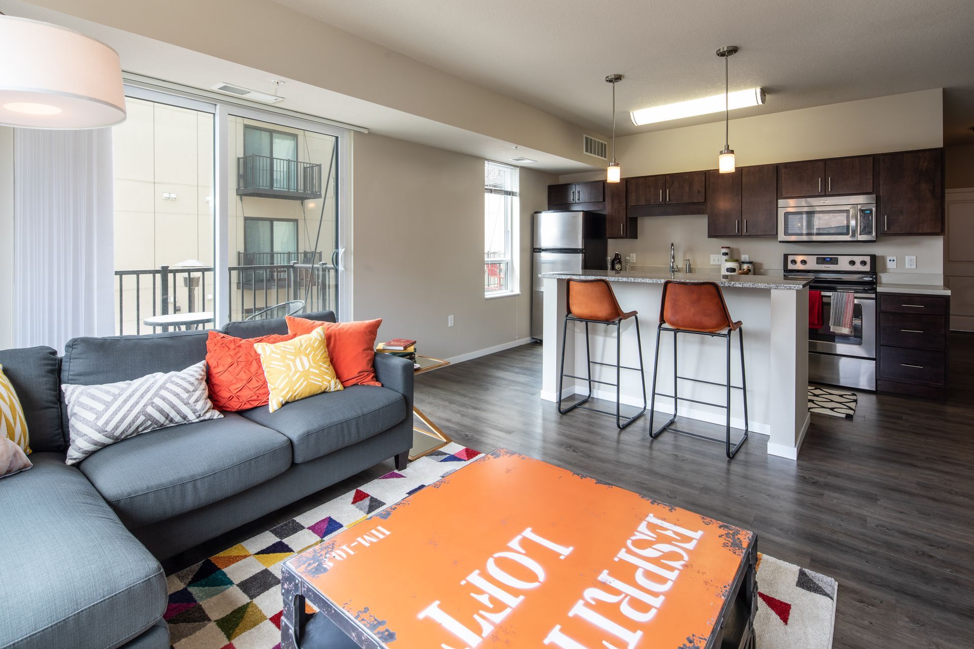 Modern apartment living room with a gray sectional, open kitchen, and a balcony.