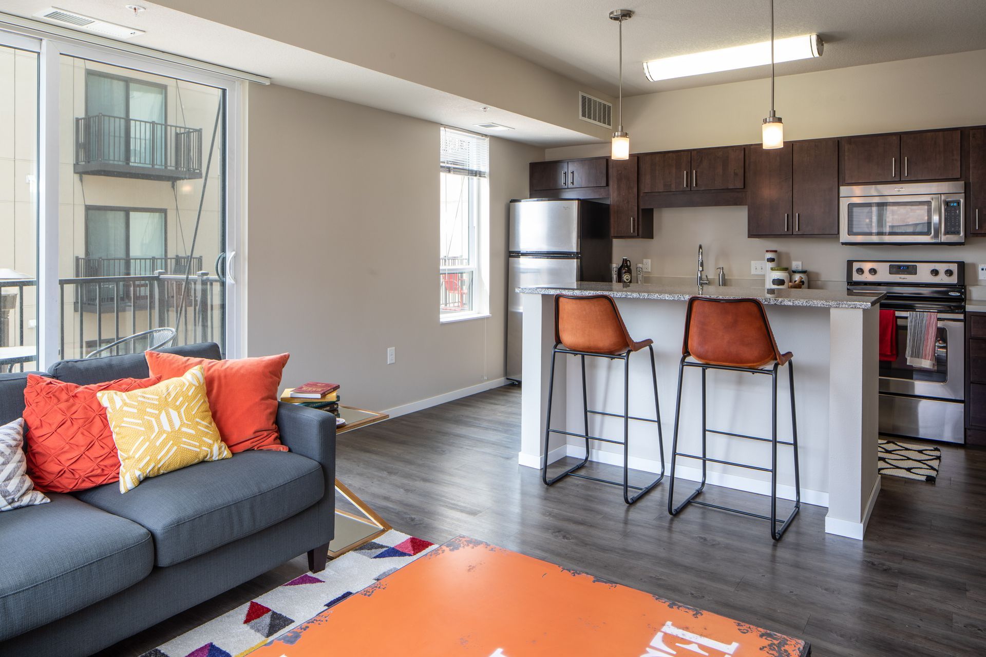 Modern apartment living room with open kitchen, balcony, and colorful decor.