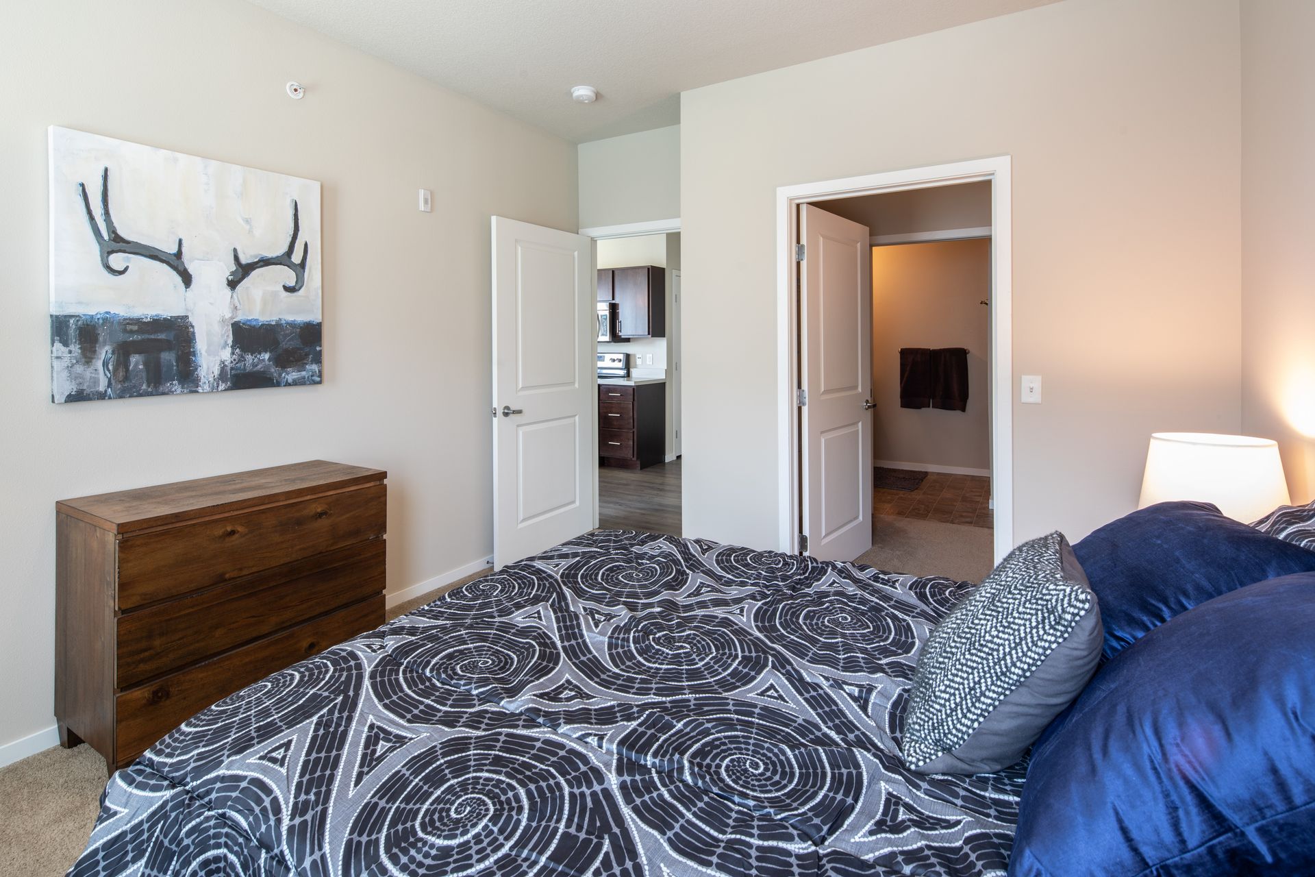 Bedroom with bed, dresser, art, and open doorways to a walk-in closet and kitchen.