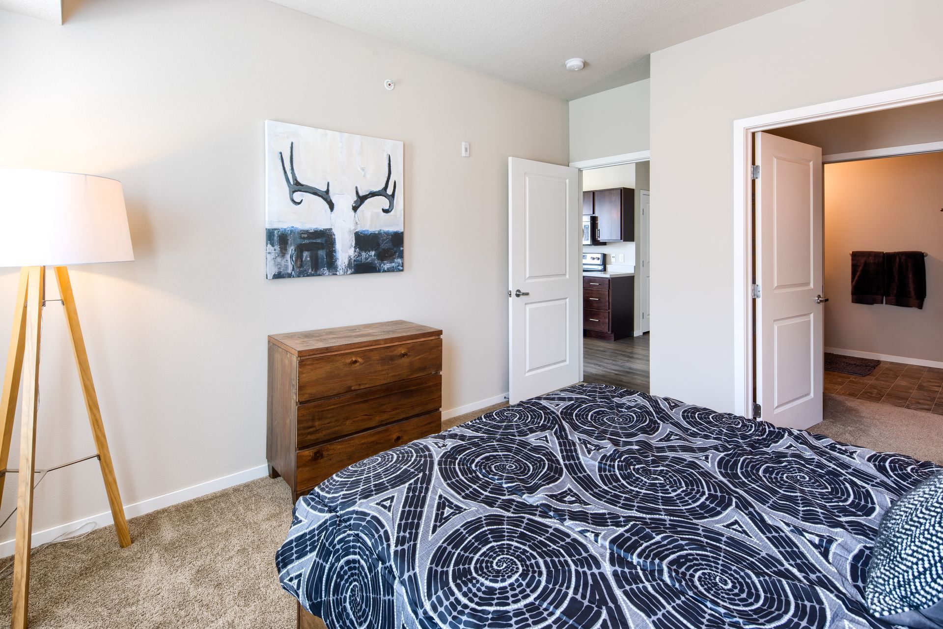 Bedroom with bed, dresser, art, and open doorways to kitchen and bathroom.