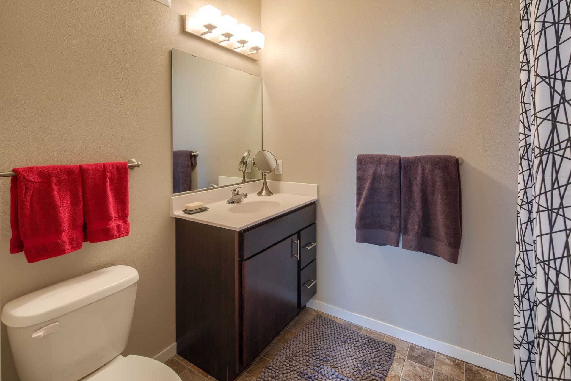 Bathroom with dark brown vanity, red and brown towels, and a white toilet.