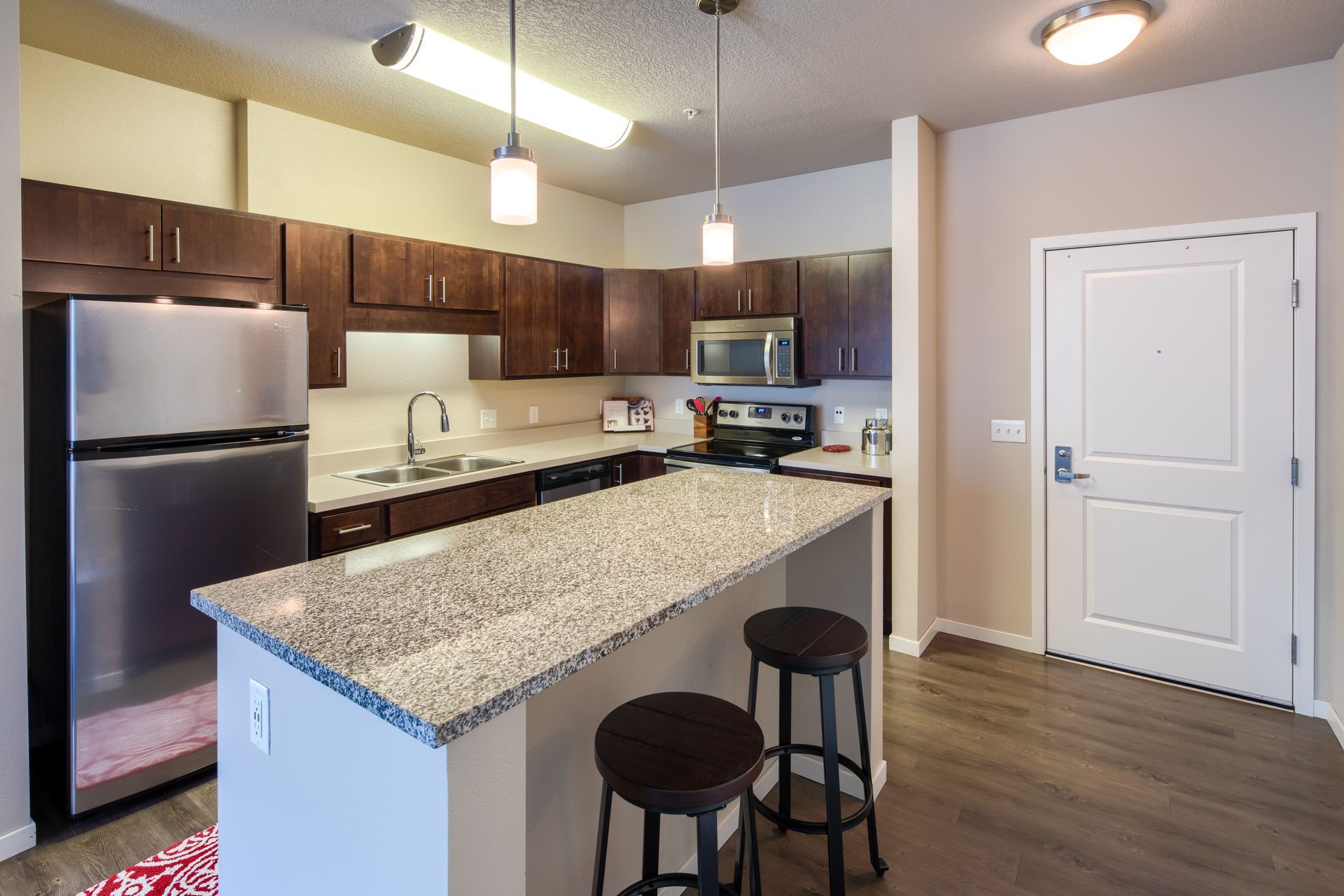Kitchen with stainless steel appliances, dark wood cabinets, granite island with stools, and white door.