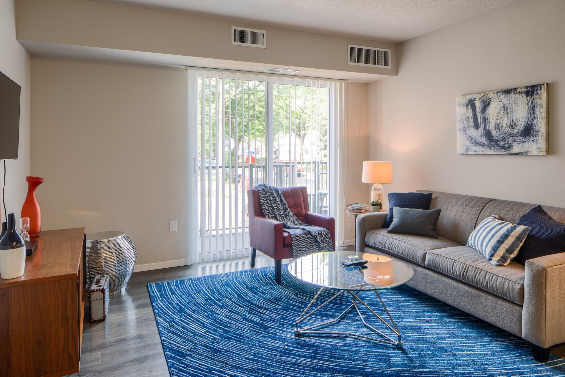 Cozy living room with a gray couch, a blue rug, and a sliding glass door leading to a balcony.