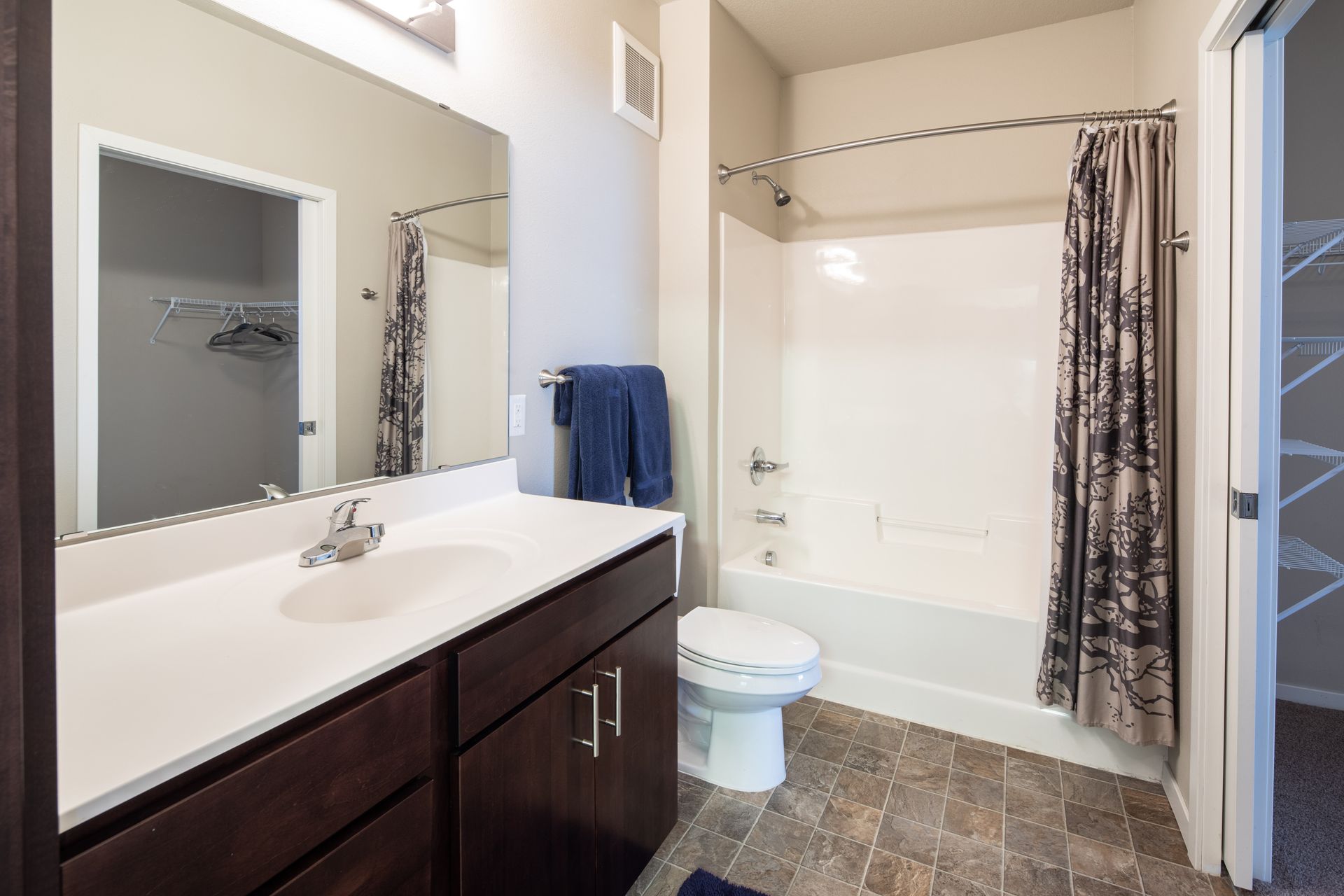 Bathroom with a dark brown vanity, white sink and toilet, shower with patterned curtain, and a closet.