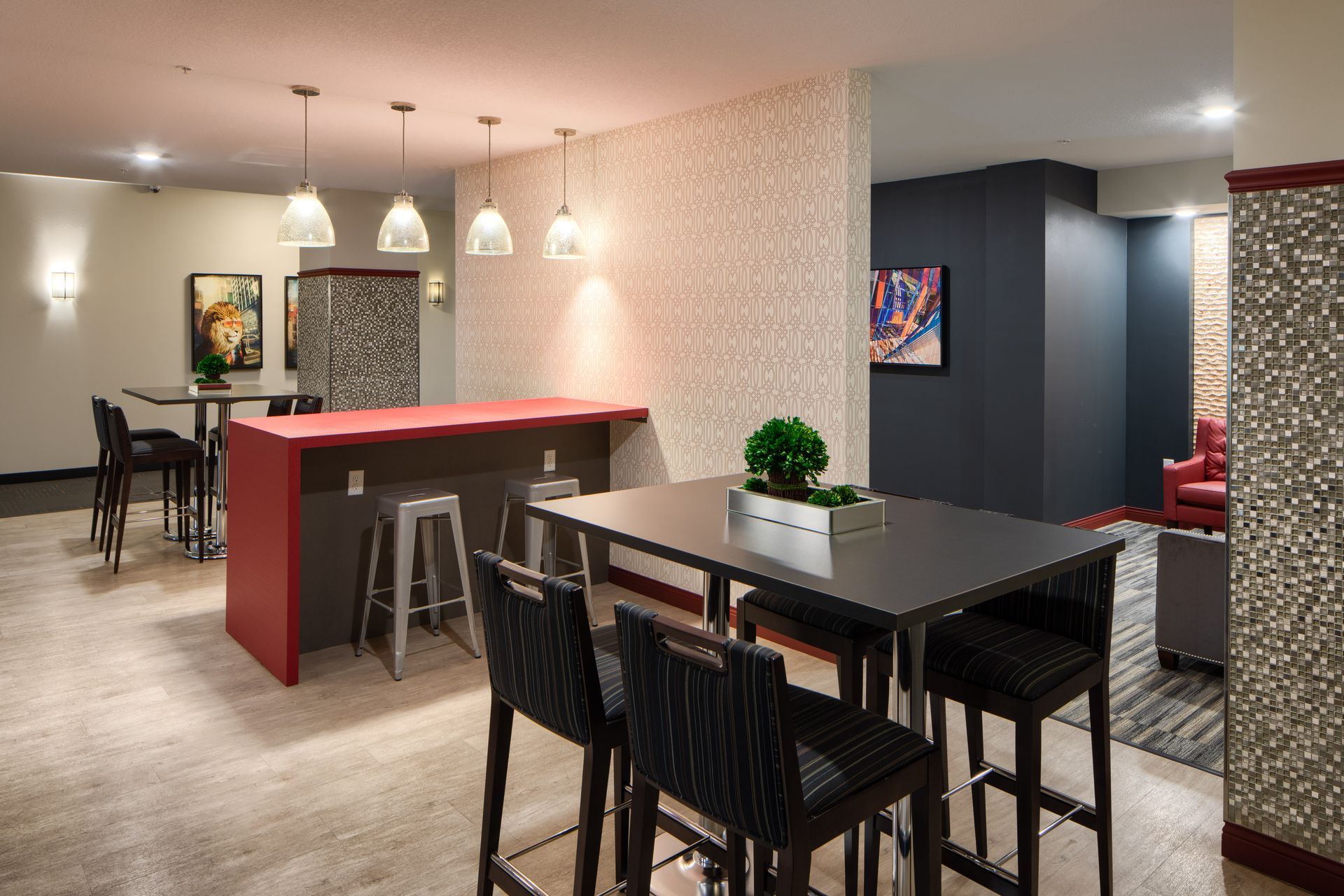 Modern lounge with tables, stools, mosaic accent wall, hanging lights, and artwork.