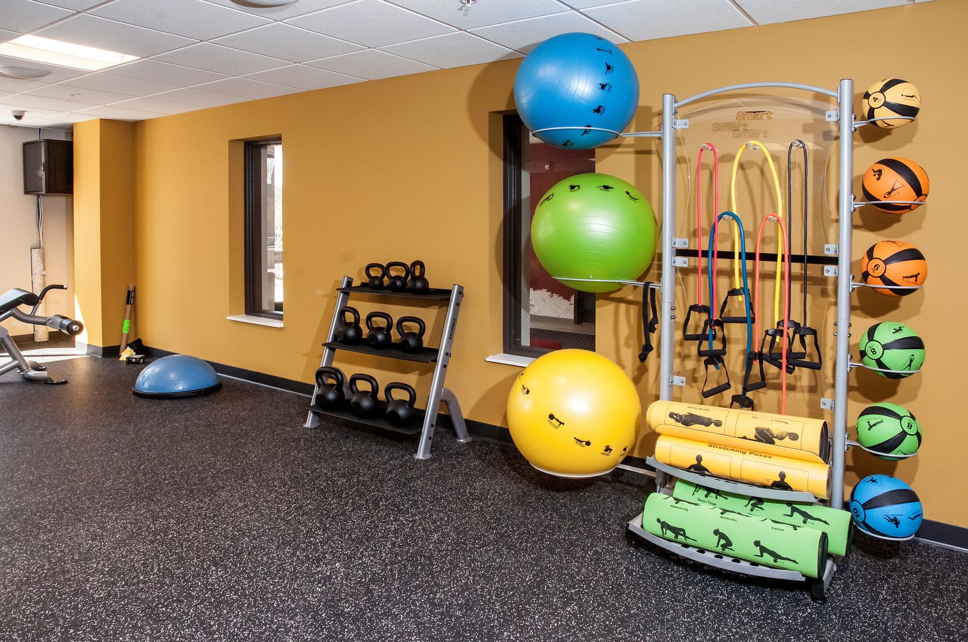 Gym with exercise balls, weights, resistance bands, and mats on a rubber floor.