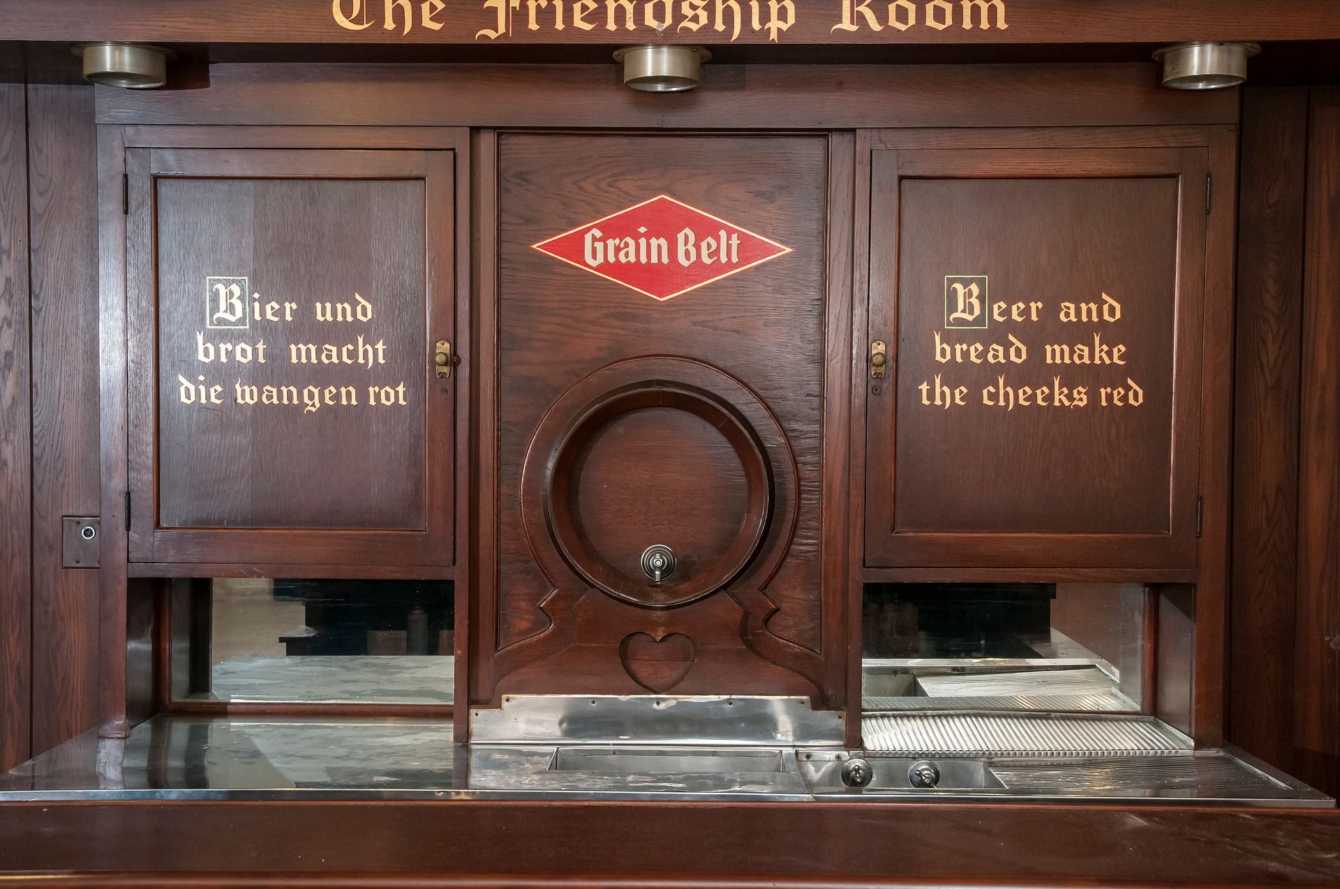 Wooden bar with beer tap, Grain Bell emblem, and German/English text.
