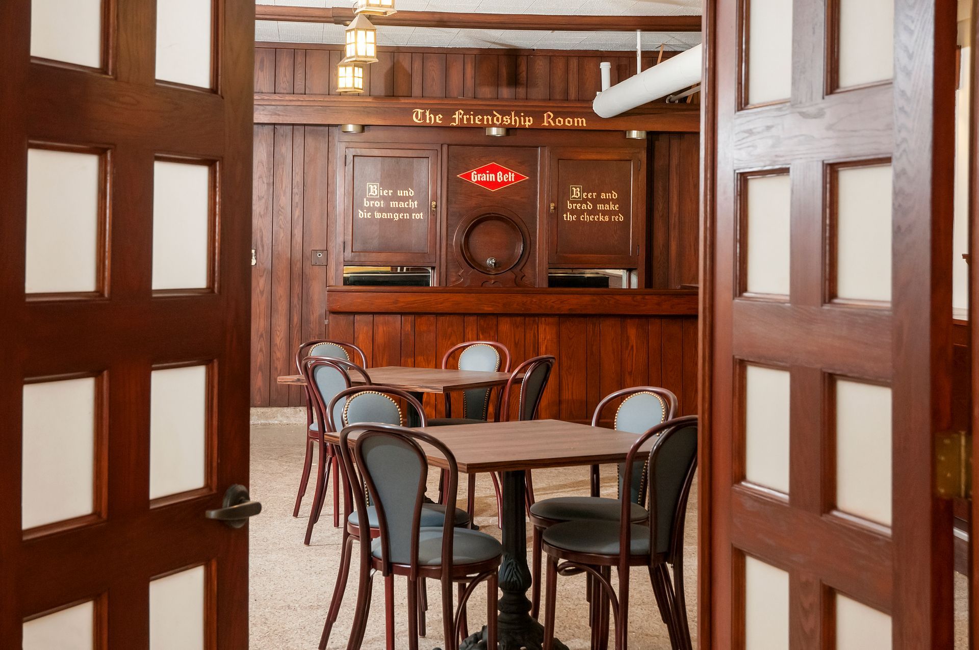 Dark wood-paneled room with tables and chairs, viewed through an open doorway.