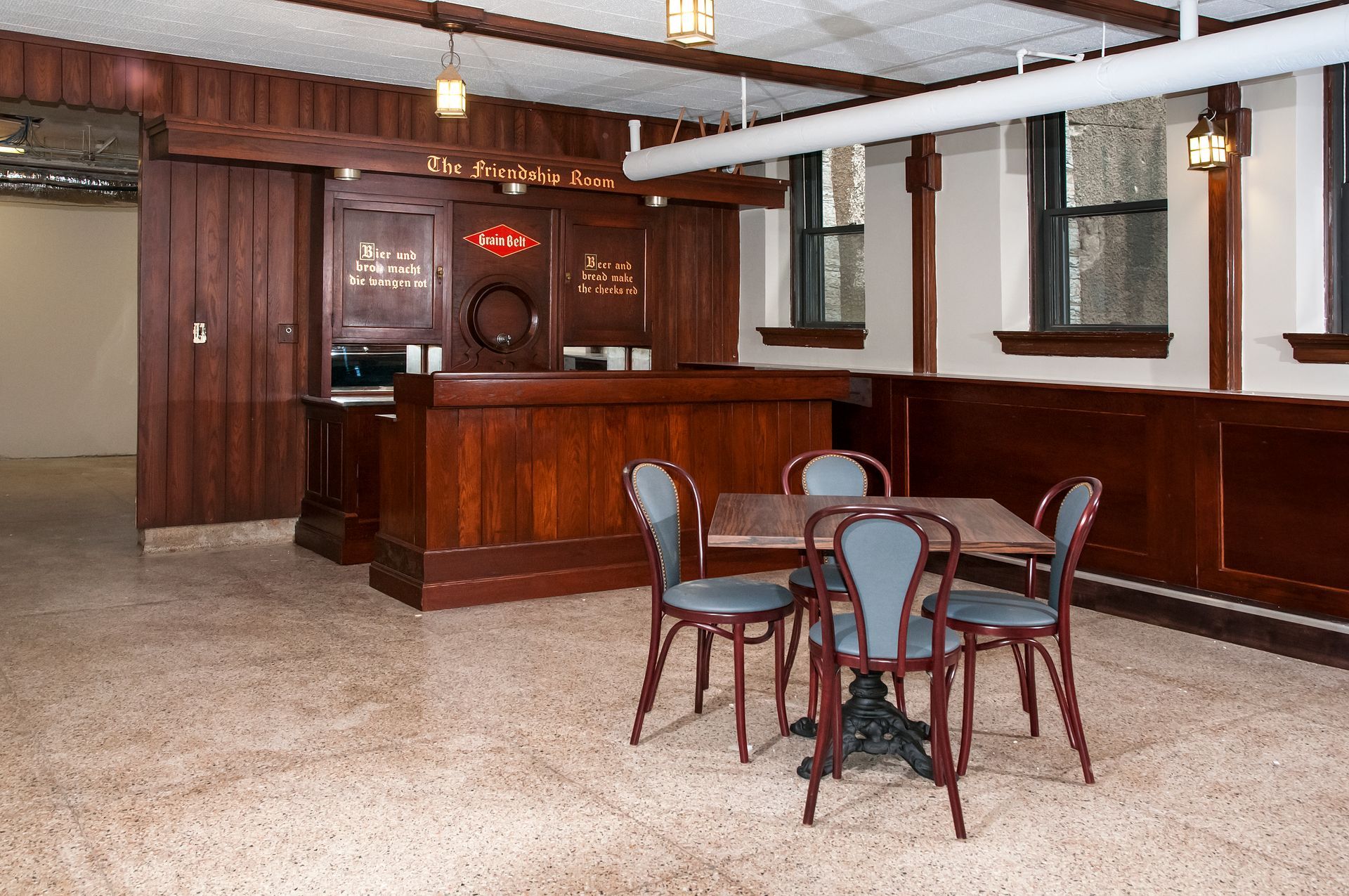 Empty room with dark wood bar and tables, windows, and terrazzo floor.