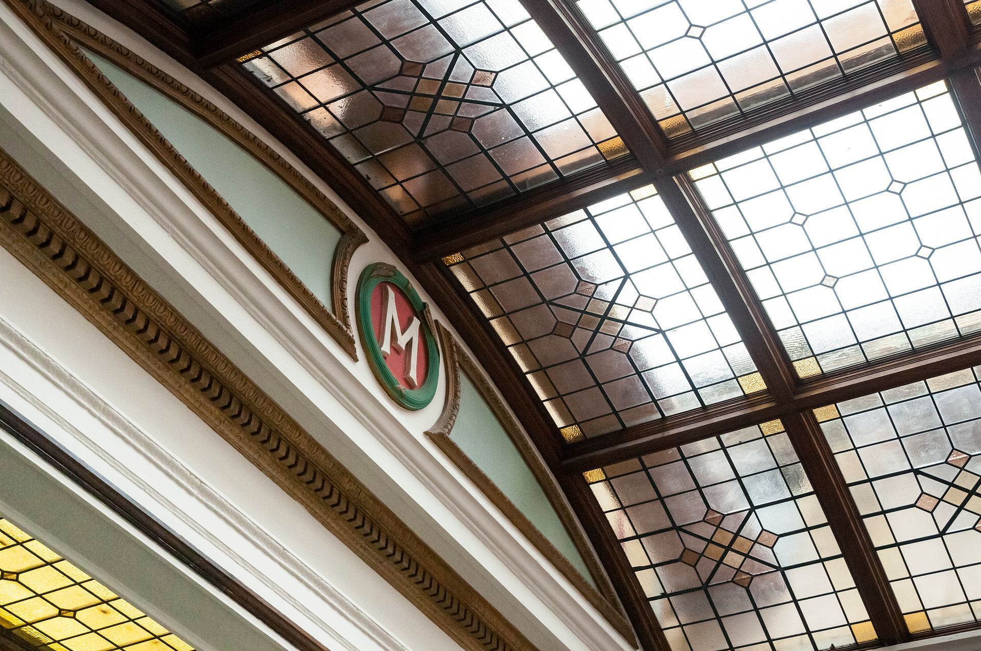 Arched ceiling with stained glass panels. Decorative molding and a circular emblem with the letter