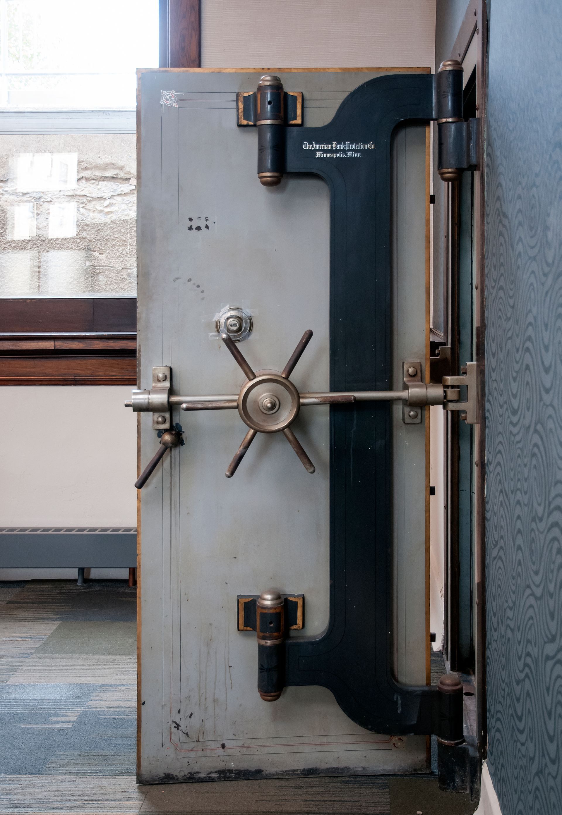 Steel bank vault door, gray and black, with a large handle and locking mechanism.