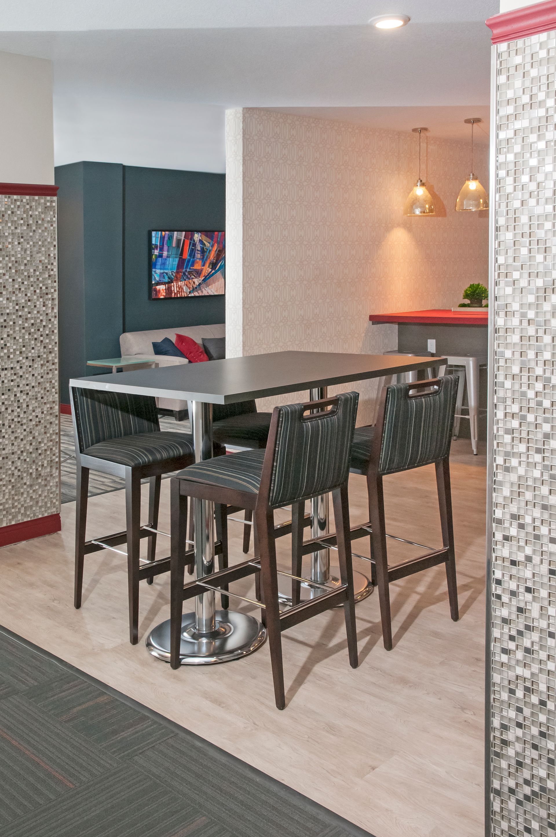 Four bar stools surround a table in a modern space. Flooring is light wood. Walls feature stone and dark blue.