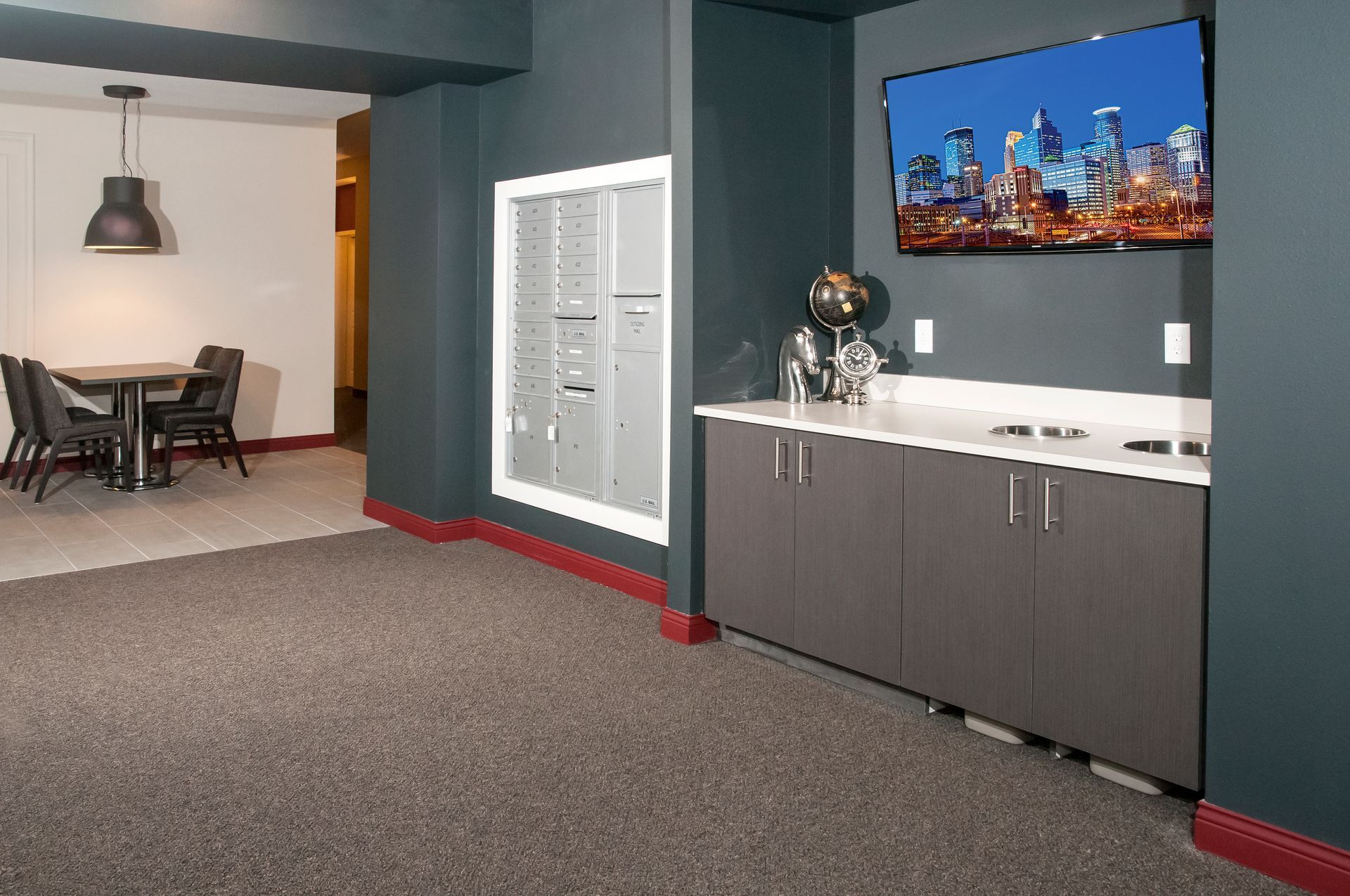 Apartment lobby with mailboxes, TV, counter, seating area, and dark blue walls.